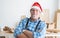 Portrait of happy Caucasian senior carpenter man with beard and mustache wearing santa hat smiling stand with arms crossed