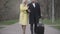 Portrait of happy Caucasian tourists strolling along the alley with travel bag. Smiling man and woman walking in park