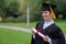 Portrait of happy caucasian woman in graduate gown holding diploma outdoors.