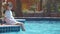 Portrait of happy child girl in white dress relaxing on swimming pool side on sunny summer day during tropical holidays