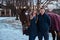 Portrait of a happy couple near to a brown horse on the ranch on a winter day.