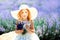 Portrait of happy cute little blonde curly girl wearing white dress and hat and holding bouquet of lavender in lavender field with