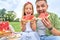Portrait of happy dad and his adorable little daughter looking at camera while eating watermelon, family having a picnic