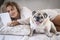 Portrait of happy dog with woman owner relaxing laying in the bed at home. Cheerful female people reading e-book with modern