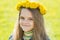 Portrait of happy eight-year-old girl with a wreath of dandelions on her head, against the background of a spring clearing
