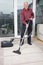 Portrait of happy elderly man cleaning rug with vacuum cleaner at home