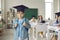 Portrait of happy elementary school graduate in academic hat standing in classroom