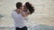 Portrait of the happy emotional couple of beautiful newlyweds tenderly hugging at the background of the sea during the