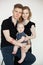 Portrait of happy family from three in black looks on white background. Dad sit on chair and hold infant baby, mom stand