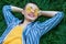 Portrait of Happy fancy young woman with short hair in casual blue striped suit, yellow shirt, glasses lying down on green grass,