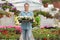 Portrait of happy gardener carrying crate with flower pots in greenhouse