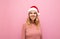 Portrait of happy girl in a santa hat on a pink background, looking away and smiling. Christmas lady in cute happy clothes