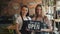 Portrait of happy girls waitresses holding we are open sign standing in cafe