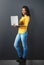 Portrait, happy indian woman standing with laptop and in wall background. Social media or networking, technology or