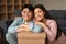 Portrait Of Happy Japanese Spouses Posing With Cardboard Box Indoors