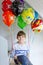 Portrait of happy kid boy with bunch on colorful air balloons on his birthday. Smiling school child having fun