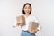 Portrait of happy korean girl holding two boxes and smiling, lookng amazed at camera, concept of shopping, white