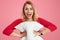 Portrait of happy light haired young woman with overjoyed facial expression, holds soft white pillow, dressed in red jumper, opens