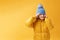 Portrait happy little girl preschooler in a winter jacket and blue hat. Yellow on a yellow background