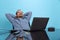 Portrait of happy looking man, computer support specialist, programmer sitting in front of laptop isolated over blue