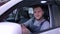 Portrait of happy male mechanic sitting behind the wheel of a new car with a smile looks at camera with the keys in hand