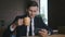 Portrait happy man businessman sitting at office, watching funny videos on a smartphone and drinking coffee or tea