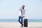 Portrait of happy man with suitcase and mobile phone standing on beach