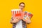 Portrait of a happy man in transparent glasses with a bucket of popcorn, keen on watching a movie, on a yellow background