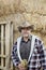 Portrait of a happy mature man with cowboy hat holding gloves in front of hay stack