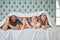 Portrait of happy parents with little children lying on bed at home under blanket. Caucasian girls bonding with their