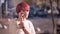 Portrait of happy pretty pink-haired girl talking on cellphone on blurred street background.