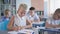 Portrait of happy pupil girl doing classwork sitting at desk on background of classmates at elementary school