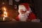 Portrait of happy Santa Claus sitting at his room at home near Christmas tree and answering Christmas letters