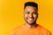 Portrait of happy satisfied Indian young man standing and looking at the camera with light smile isolated on yellow