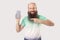 Portrait of happy satisfied middle aged bald bearded man standing with mobile smart phone pointing at empty screen and looking