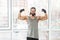 Portrait of happy satisfied sporty young adult muscular trainer man with curly long hair standing with raised heavy arms, showing