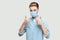 Portrait of happy satisfied successful handsome young man with surgical medical mask in light blue shirt standing, thumbs up and