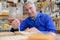 Portrait happy senior carpenter varnishing wood in workshop