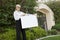 Portrait of a happy senior female agent hammering sign board in lawn