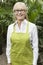 Portrait of a happy senior female gardener with apron standing in botanical garden