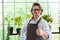 Portrait of happy senior man gardening wearing glasses and denim apron. Showing thumbs up smiling and standing with plant shelf