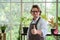 Portrait of happy senior man gardening wearing glasses and denim apron. Showing thumbs up, smiling and standing with plant shelf