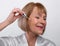 Portrait of happy senior woman in dressing gown applying face serum with dropper on light studio background