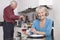 Portrait of happy senior woman with wine glass while husband cooking food in kitchen