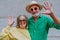 Portrait of happy seniors couple in colourful clothes waving at camera.