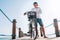 Portrait of a happy smiling barefoot man dressed in light summer clothes and sunglasses riding a bicycle on the wooden sea pier.