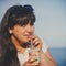 Portrait of happy smiling beautiful overweight young woman in white T-shirt drinking sweet coffee through a straw outdoors beach