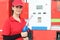 Portrait of happy smiling beautiful woman gas station attendant in red uniform holding a fuel petrol pump nozzle against at gas