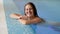 Portrait of happy smiling brunette woman in white swimsuit relaxing in swimming pool and looking in camera