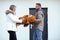 Portrait of happy smiling cute couple in casual upper garments stand holding huge orange teddy bear and paperboard box.